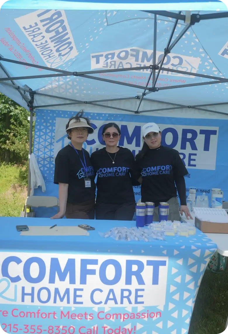 Three Comfort Home Care team members standing at a branded community outreach event booth
