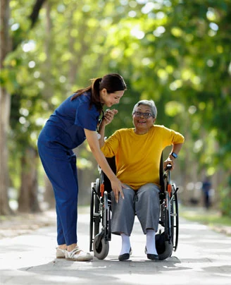 Compassionate Home Caregiver Assisting Senior Outdoors | Comfort Home Care Home caregiver assisting a smiling senior woman in a wheelchair outdoors