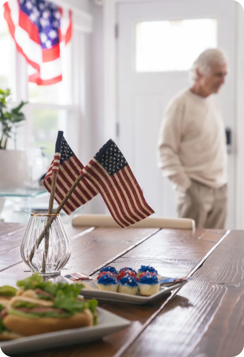 Senior Enjoying a Patriotic Celebration at Home | Comfort Home Care American flags and patriotic refreshments arranged on a table with a senior man at home