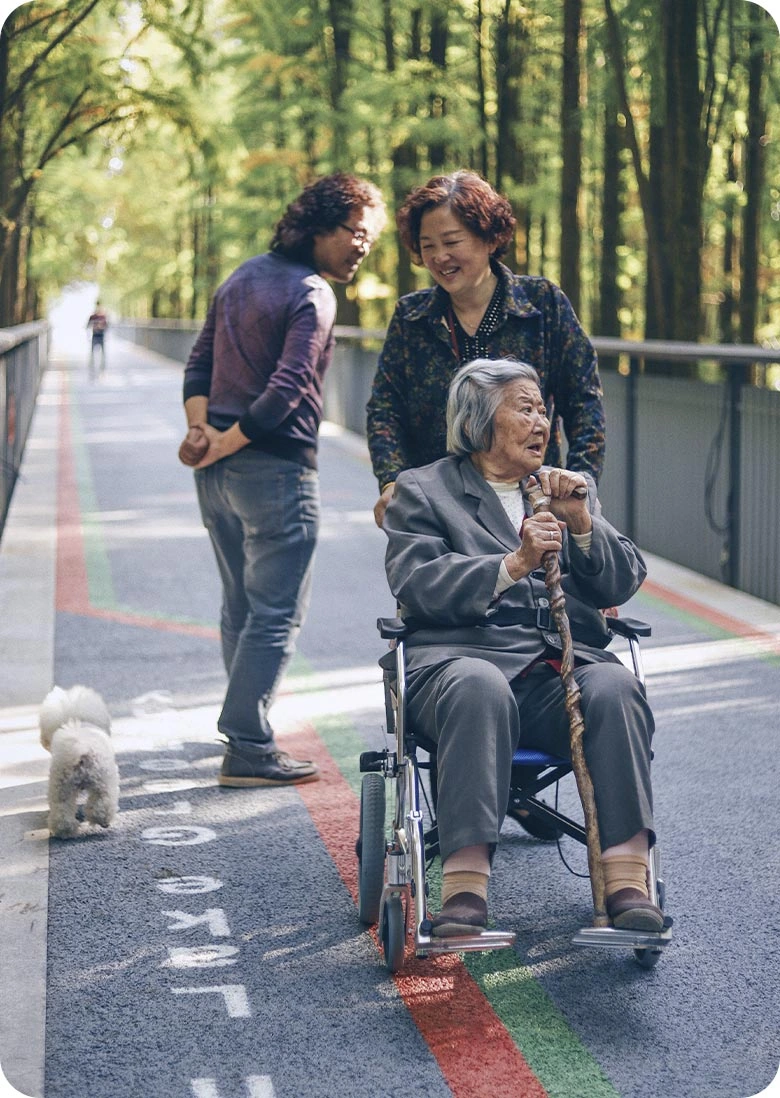 Outdoor Companion Care for a Senior Woman in a Wheelchair | Comfort Home Care Senior woman in a wheelchair enjoying an outdoor walk with two companions